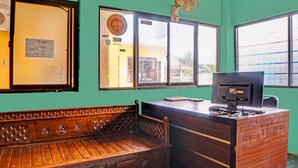 Una habitación con un banco de madera, un escritorio con computadora y una ventana con ventilador.