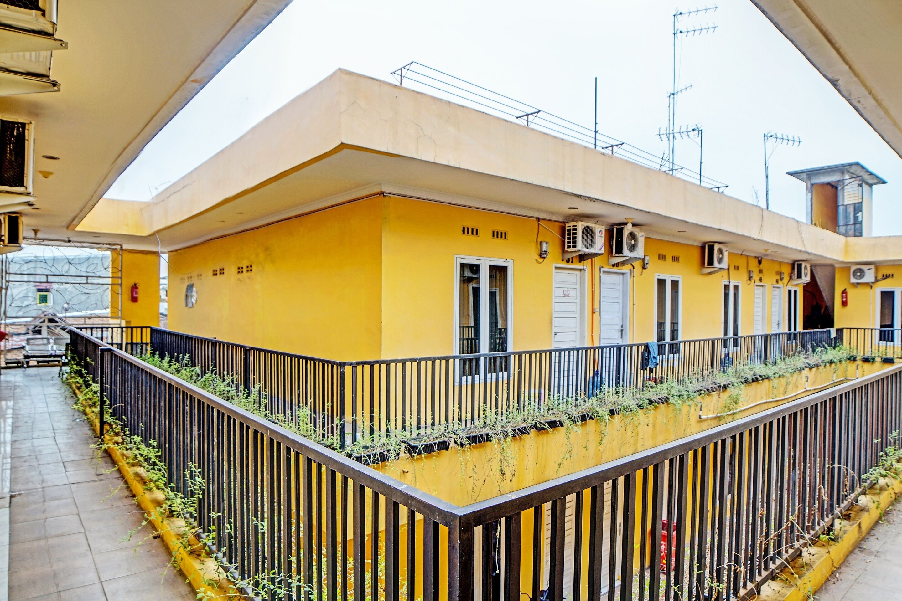 A yellow building with multiple air conditioning units, a gated entrance, and a small balcony with plants.