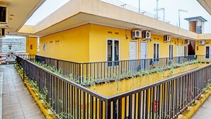 Un edificio amarillo con varias unidades de aire acondicionado, una entrada con reja y un pequeño balcón con plantas.