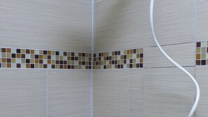 Un espace douche équipé d’un pommeau de douche à main, d’un mur carrelé et d’un sol de douche également carrelé.