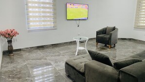 A modern living room with a grey sofa, a glass coffee table, a black armchair, and a TV mounted on the wall. - The Boaz Executive Place (Kumasi)