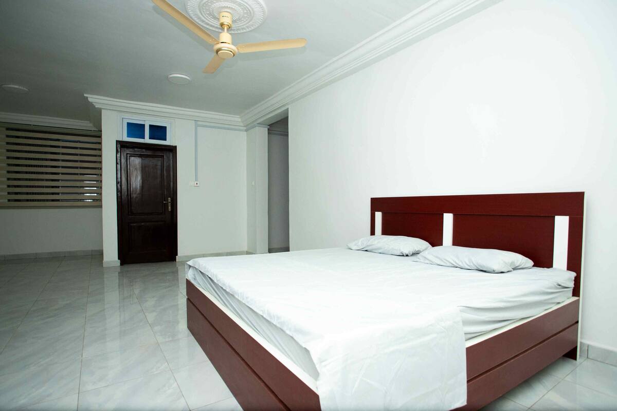 Quarto com cama, ventoinha no teto e porta.