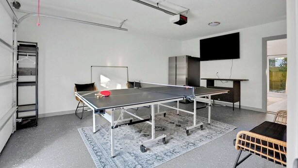 A ping pong table in a room with a white wall, a flat-screen TV, and a ladder. - New Construction in Historic Linconville (Saint Augustine)