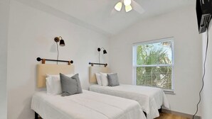 A room with two beds, each with a headboard and pillows, a ceiling fan, and a window with blinds. - New Construction in Historic Linconville (Saint Augustine)