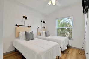 Ein Zimmer mit zwei Betten, jeweils mit Kopfteil und Kissen, einem Deckenventilator und einem Fenster mit Jalousien.