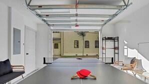 A ping pong table with a net in a room with a view of a building outside. - New Construction in Historic Linconville (Saint Augustine)