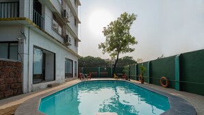 Una piscina con zona de descanso, rodeada por un edificio de pared de ladrillo y un árbol.