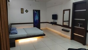 Un dormitorio con cama, televisor montado en la pared, espejo y una puerta.