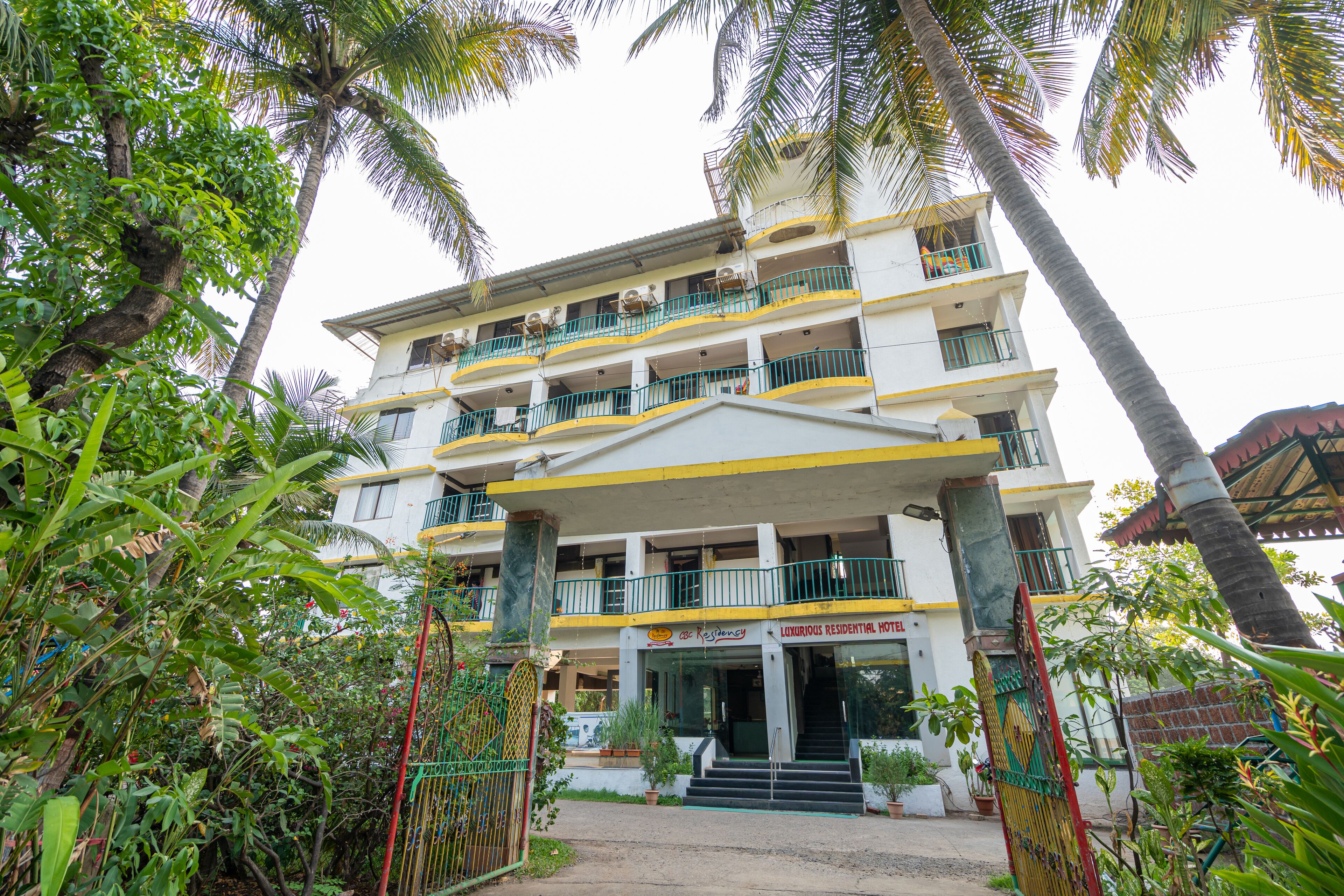 Un hotel de varios pisos con balcones, rodeado de exuberante vegetación y palmeras.