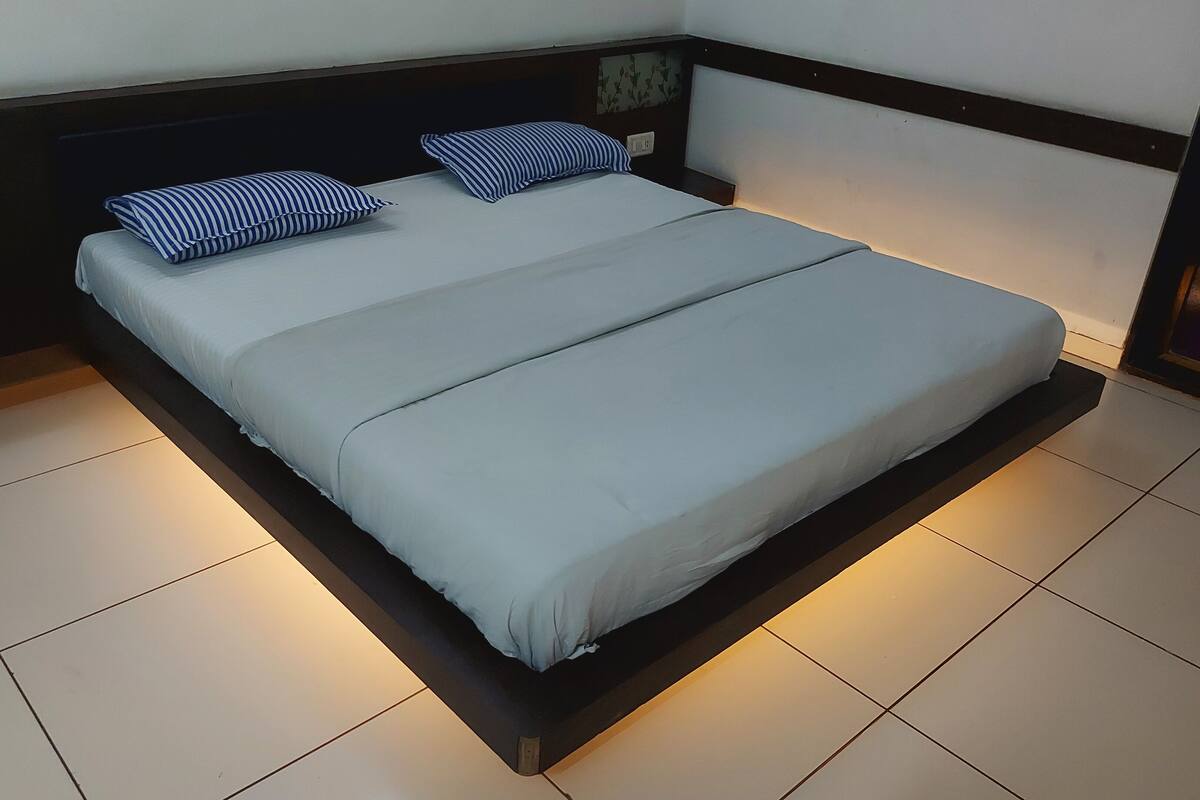 A bed with a white mattress and two blue and white striped pillows, a wooden headboard, and a tiled floor.