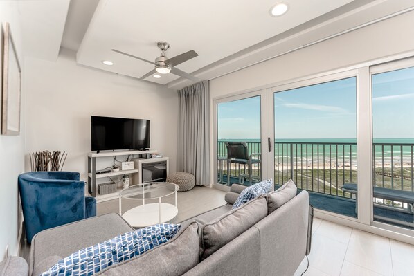 Una sala de estar moderna con un sofá, televisor y un balcón con vistas a la playa.