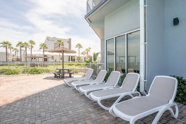 A patio with sun loungers, a picnic table, and a small umbrella.