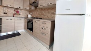 Eine moderne Küche mit hellen Holzschränken, einem weißen Kühlschrank, einem Herd und einem Backofen.