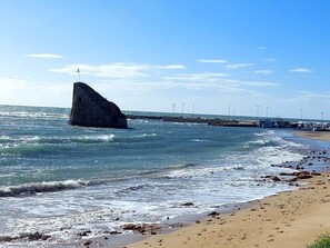 Eine Küstenansicht mit einer großen Felsformation, einem Sandstrand und einer Pier mit Booten.