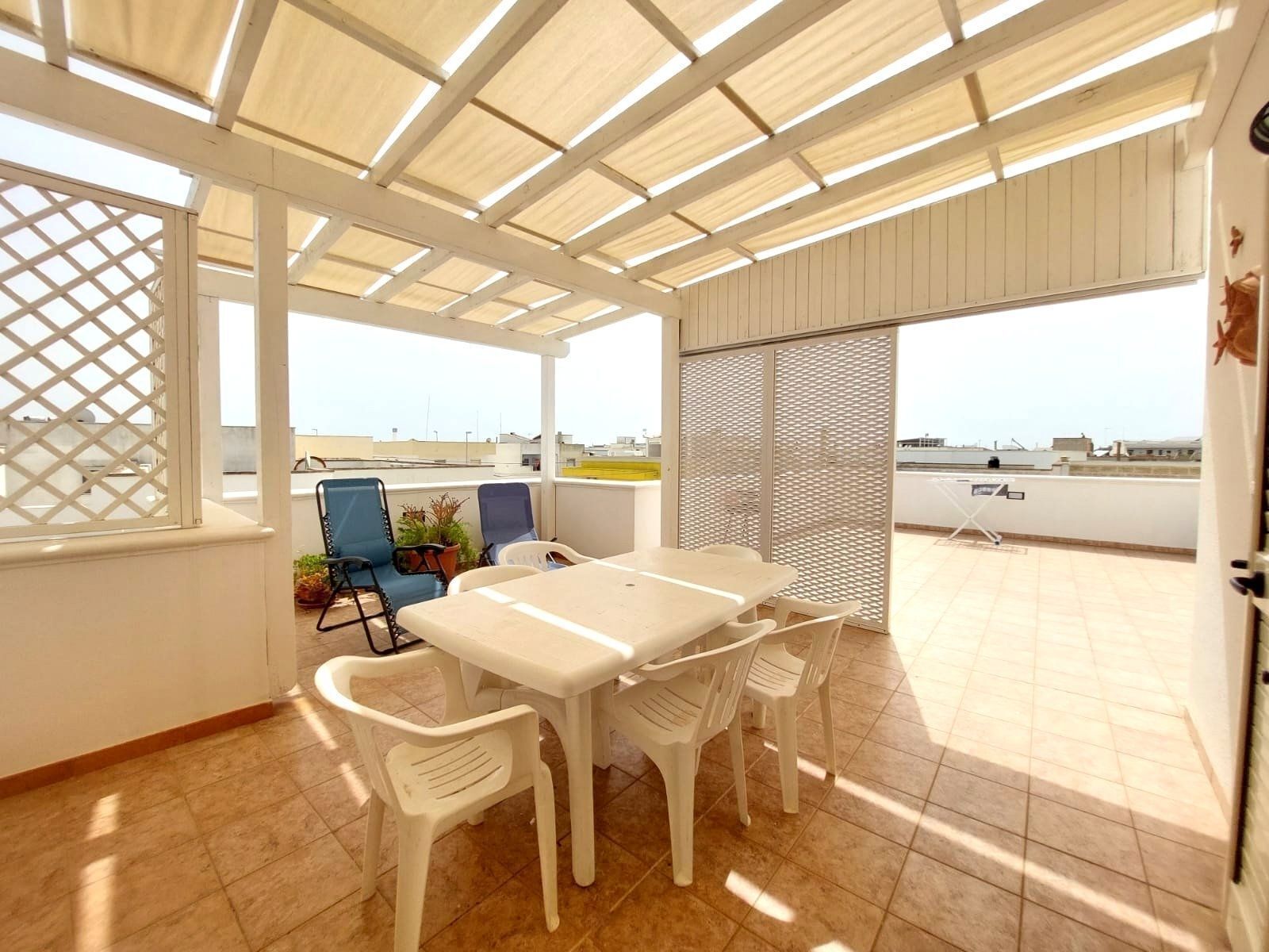 A covered patio with a table and chairs, a view of the cityscape, and a lattice window.