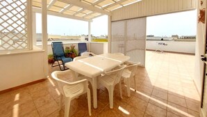 Eine überdachte Terrasse mit Tisch und Stühlen, Blick auf die Stadt und ein Gitterfenster.
