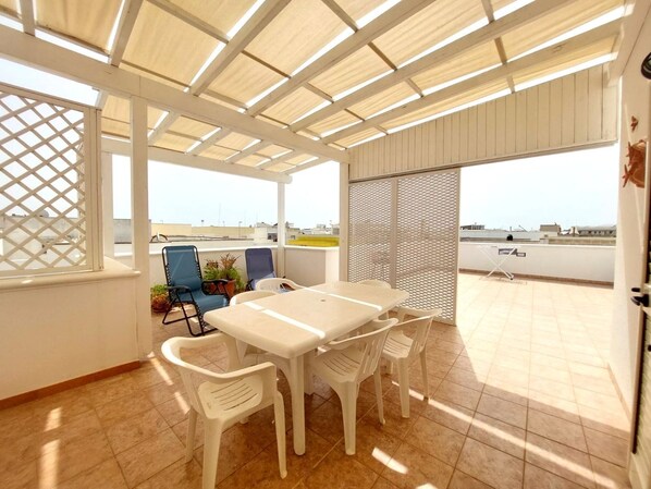 A covered patio with a table and chairs, a view of the cityscape, and a lattice window.