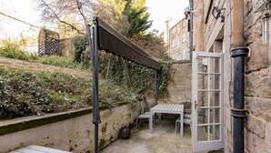 Ein Steinhaus mit überdachter Außenbestuhlung, einer Tür und einem kleinen Tisch.