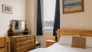 Una camera da letto con un letto di legno, una cassettiera, un comodino, una finestra con tende e un quadro appeso al muro.