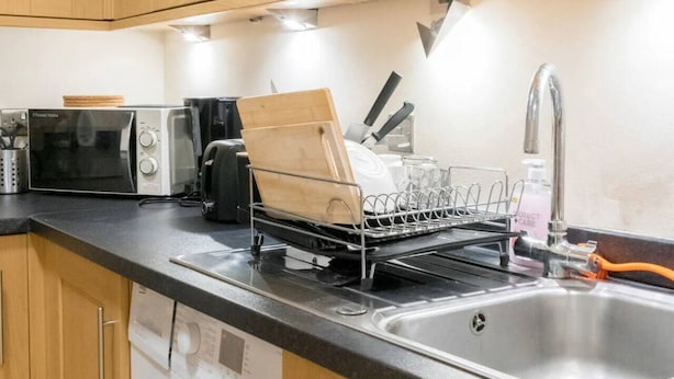 Una cucina compatta con mobili in legno, un forno a microonde, un espositore per piatti, un lavandino e una lavatrice.