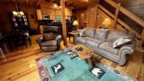 A cozy log cabin interior with a leather armchair, a sofa, a coffee table, and a patterned rug.