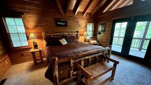 A cozy log cabin bedroom with a large bed, wooden benches, and two bedside lamps.