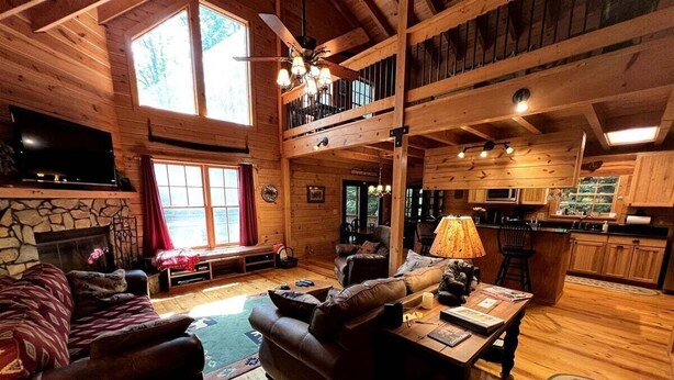 A cozy cabin interior with a fireplace, leather sofas, a dining area, and a kitchen.
