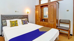 A neatly made bed with a blue bedspread and decorative pillows, a wooden wardrobe with a mirror, and a single chair. - SPOT ON 91471 Syariah Wisma Uin Walisongo (Semarang)