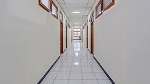 A long, narrow hallway with white tiled floors and wooden-framed windows on both sides. - SPOT ON 91471 Syariah Wisma Uin Walisongo (Semarang)