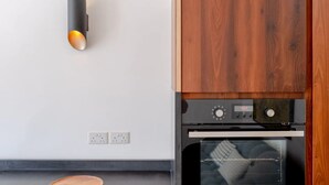 A kitchen with a built-in oven, a wall-mounted light, and a wooden cabinet. - Stylish & Light Victorian 2BD Flat - Holland Park (London)