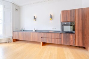 Une cuisine moderne avec des meubles en bois, un four encastré et deux lampes fixées au mur.
