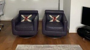 Un salon avec deux fauteuils en cuir, un lustre moderne et deux tableaux abstraits accrochés au mur.