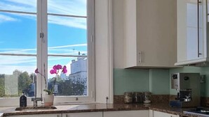 Une cuisine avec des meubles blancs, une fenêtre donnant sur le ciel et une orchidée en pot posée sur le rebord de la fenêtre.