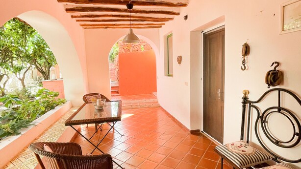 A corridor with a tiled floor, a table with chairs, a bench, and a hanging light fixture.