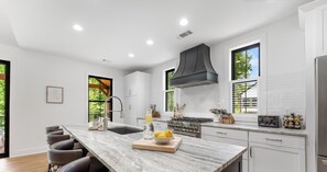 A modern kitchen with a marble countertop, stainless steel appliances, and a large window providing natural light. - Luxury Helen Cabin Near Wineries, Chef’s Kitchen, 4 Ensuites, Hot Tub, Game Room (Sautee Nacoochee)