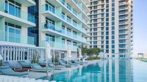 A modern hotel with a pool area, multiple balconies, and a clear view of the surrounding cityscape.