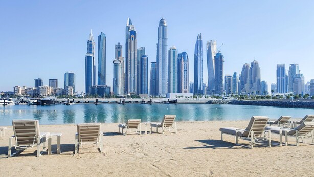 A beach with lounge chairs and a marina with boats.