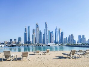 Ein Strand mit Liegestühlen und eine Marina mit Booten.