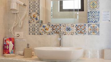 Casa de banho com lavatório branco, um porta-toalhas com toalhas dobradas, secador de cabelo e um painel de azulejos decorativo.