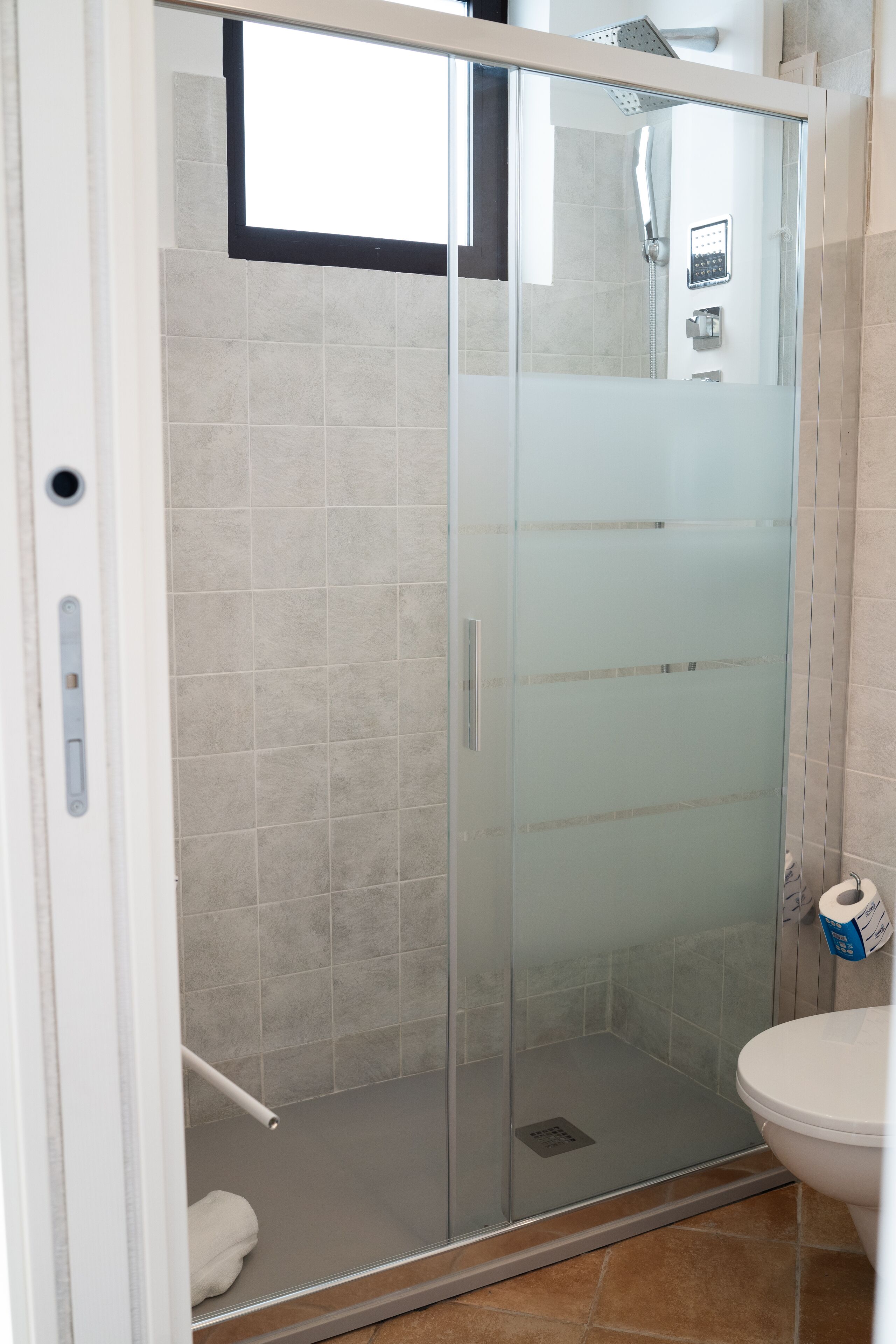A glass-enclosed shower stall with a white toilet and a towel rack.