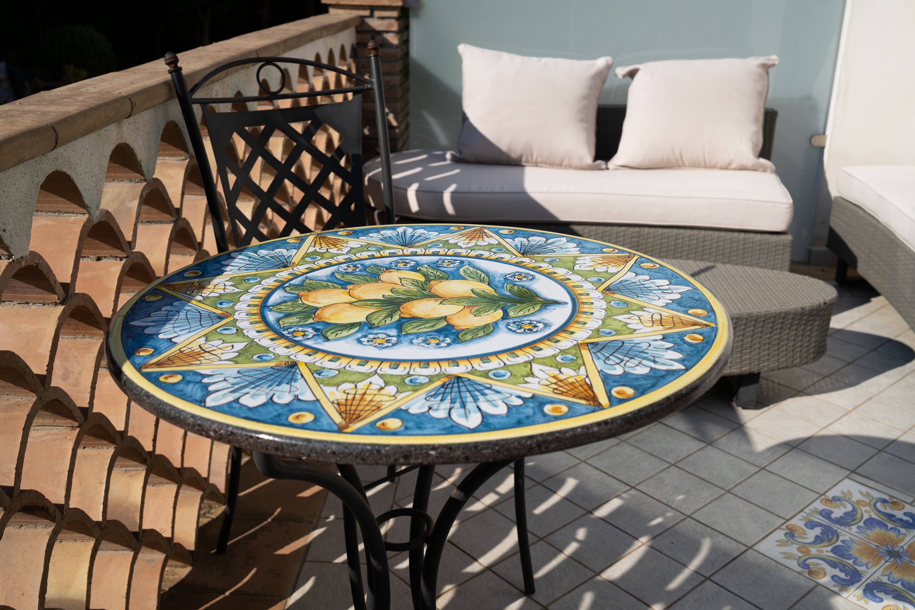 A round table with a colorful floral pattern, a black metal chair, and a white sofa with cushions.