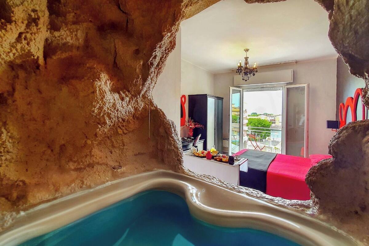 A room with a pool, a bed, a chandelier, and a view of the city.