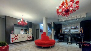 Een moderne hotel lobby met een receptiebalie, een rode bank, een bar en een kroonluchter.