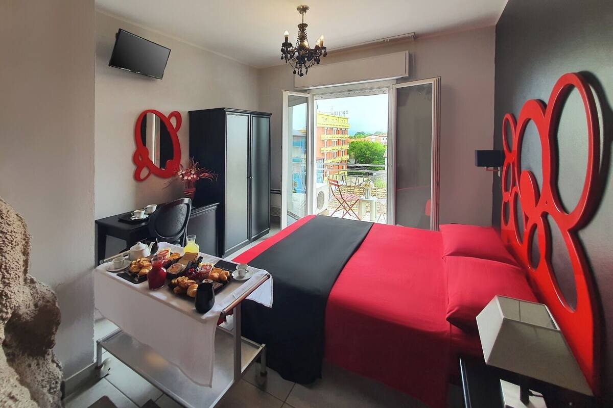 A hotel room with a bed, a desk with breakfast, a TV, and a balcony with a view.