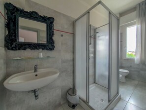 Un bagno moderno con doccia vetrata, un lavandino bianco e un grande specchio con cornice decorata.