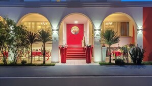 Een hotelgevel met een rode deur, gebogen ramen en een trap naar de ingang.