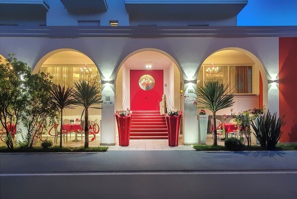 L'ingresso di un hotel con una porta rossa, finestre ad arco e una scalinata che conduce all'ingresso.