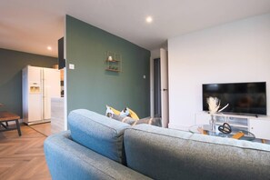 Ein modernes Wohnzimmer mit einem grauen Sofa, einem Flachbildfernseher und einem weißen Kühlschrank.