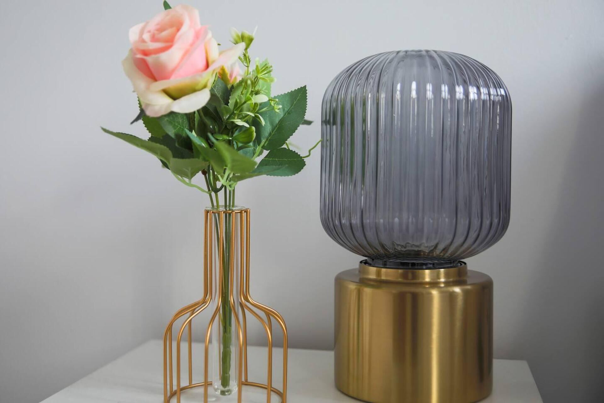A vase with a pink rose and green leaves, and a cylindrical object with a ribbed texture.