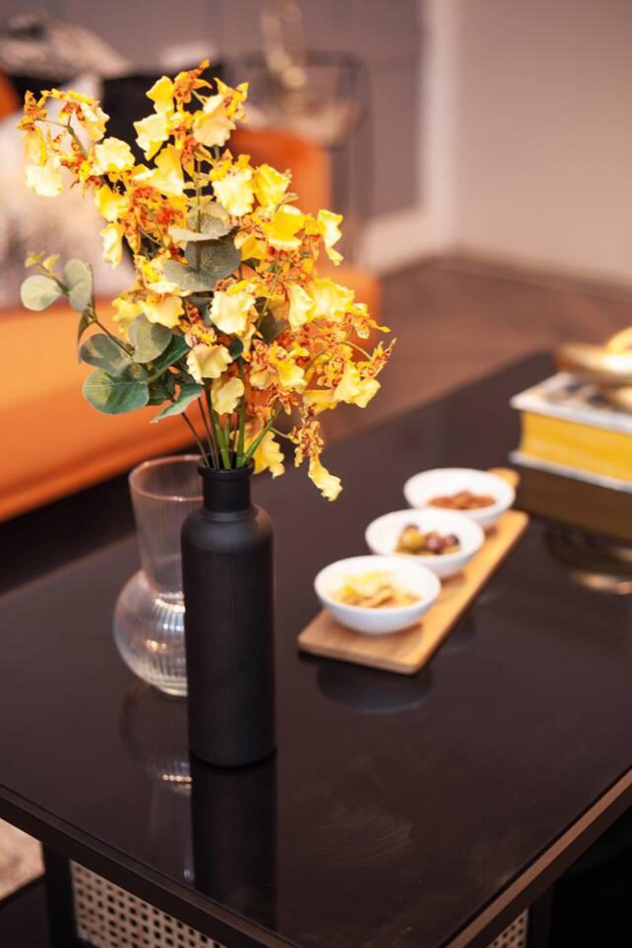 A dining table with a vase of yellow flowers, a glass, and bowls of food.